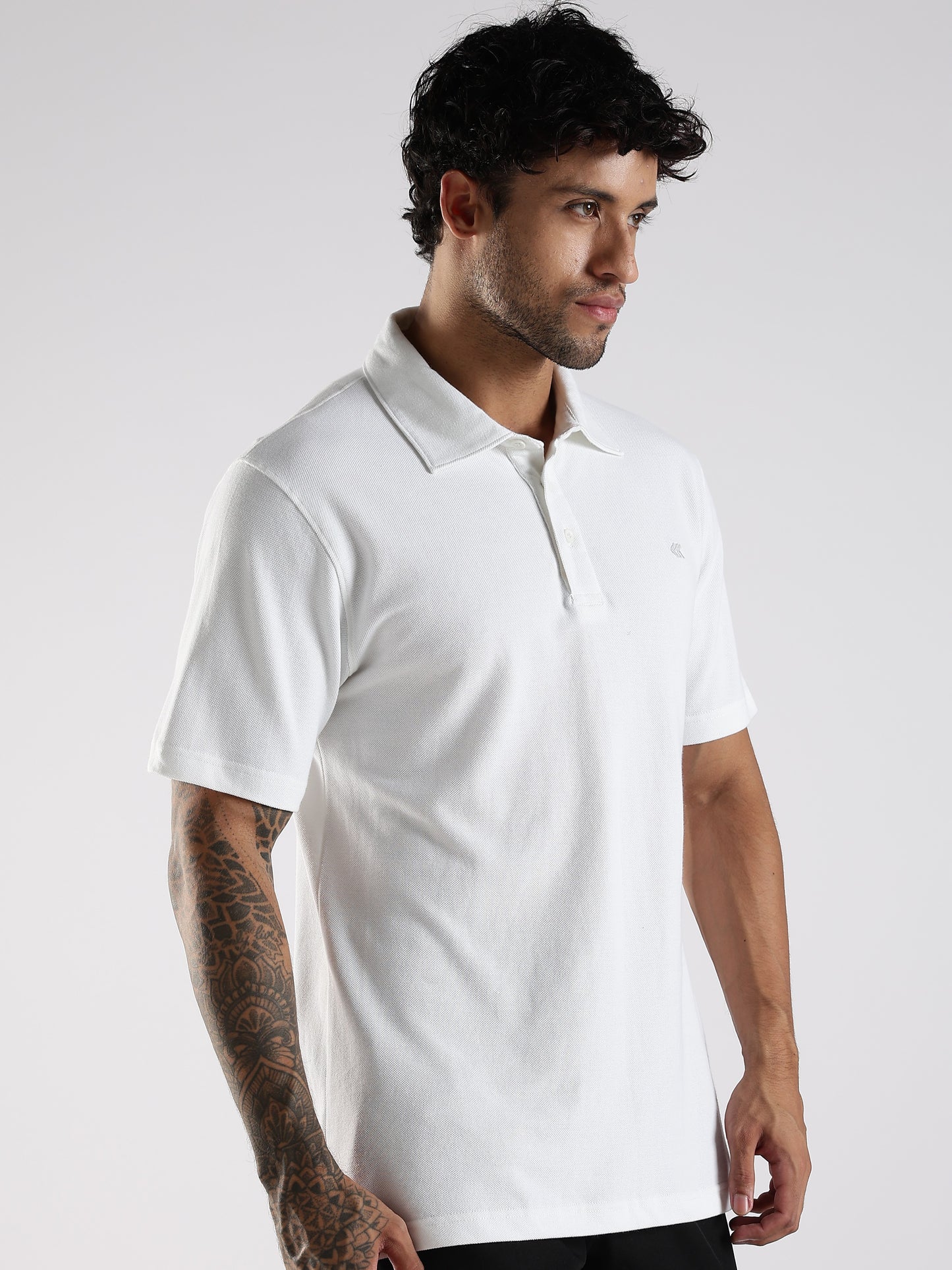Man wearing a white polo shirt with fused collar, collar-stand and embroidered logo against a plain background