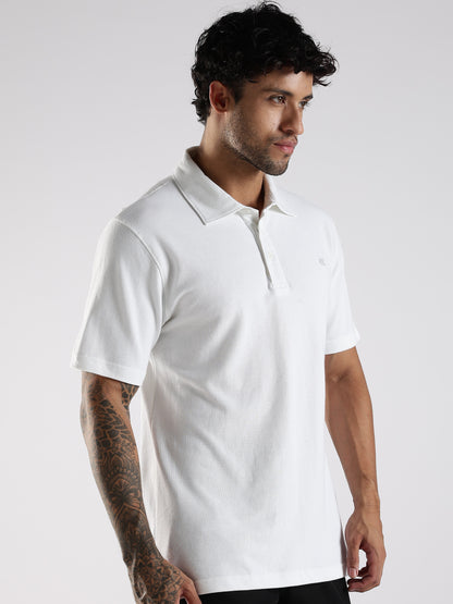 Man wearing a white polo shirt with fused collar, collar-stand and embroidered logo against a plain background