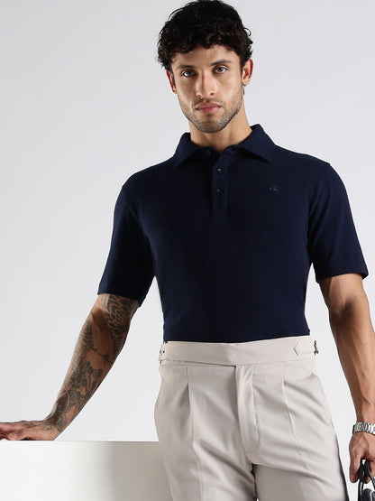 Man wearing a navy blue polo shirt and beige pants against a white background