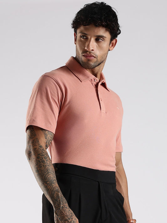 Man wearing a pink polo shirt and black pants on a light gray background