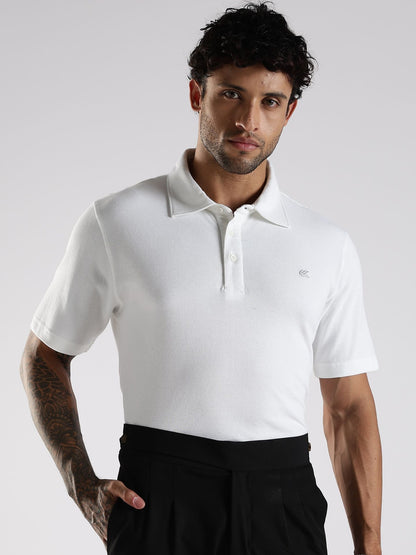 Man wearing a white polo shirt with a small logo on a plain background